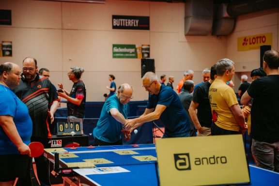 Tischtennis-Turnier mit mehreren Spielern und Tischen in einer Sporthalle.